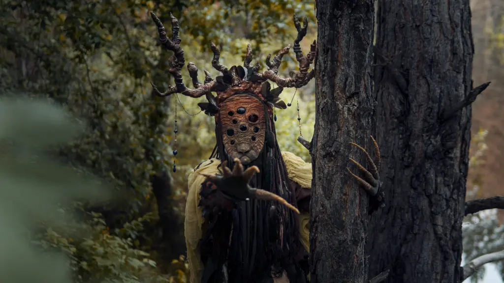 A person wearing a scary wooden mask in a forest