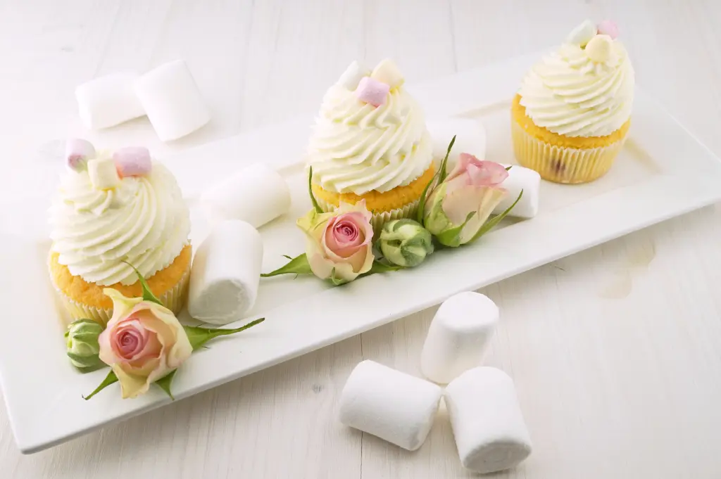 Tree cupcakes topped with a yellow cream with yellow roses and white marshmallows on a rectangular plate