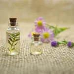 Two different vials of essential oil placed in front of pink flowers