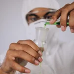 A man dressed in white laboratory clothes pouring a green liquid from a test tube to a vial