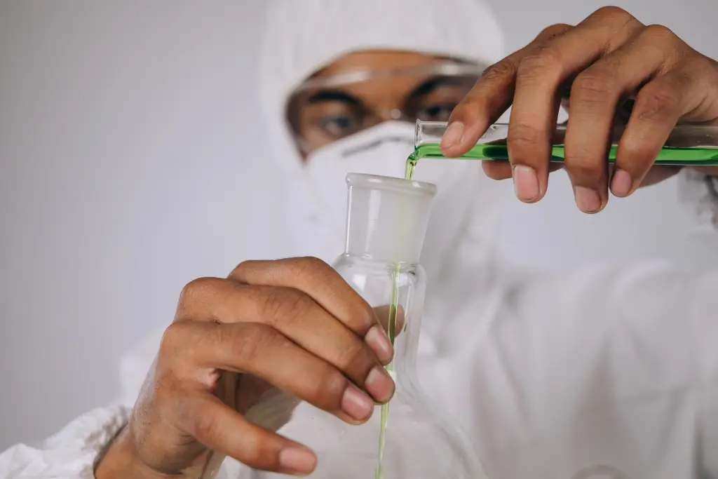 A man dressed in white laboratory clothes pouring a green liquid from a test tube to a vial